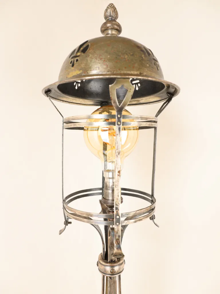 Tall Arts & Crafts-style silver-plated table lamp, c.1900&ndash;1920, featuring a pierced fleur-de-lis domed canopy, decorative floral finial, open cylindrical lantern framework, elegant scrolling metal supports and a circular wooden base, retaining a beautifully aged silver patina.