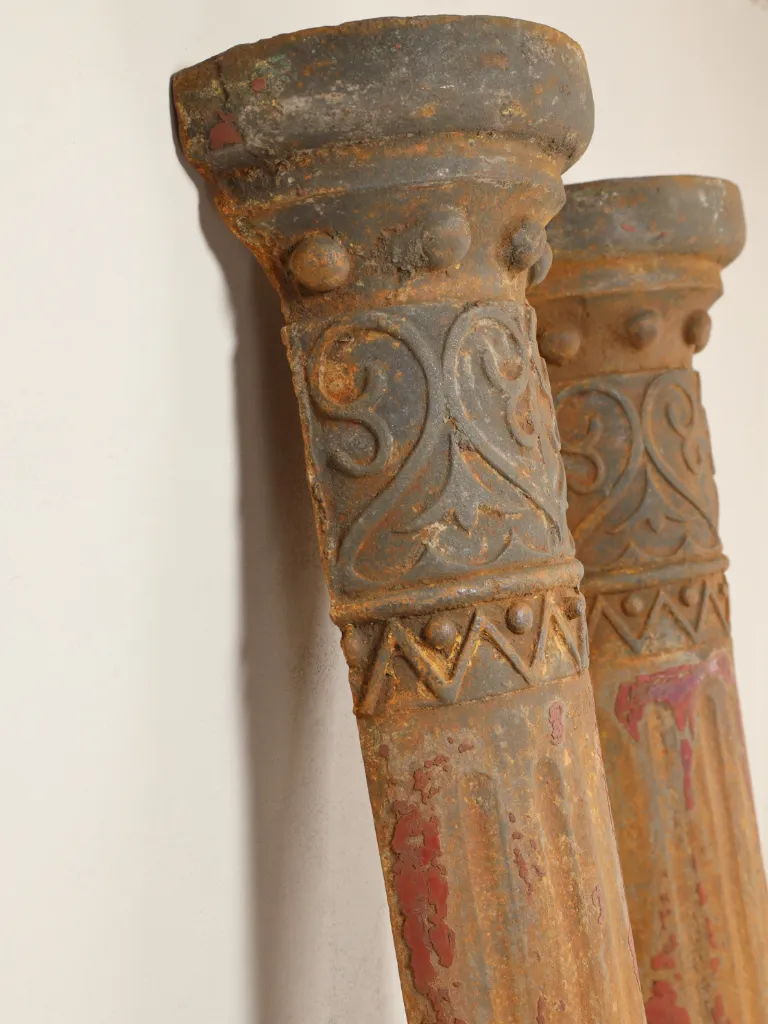 Pair of English Victorian cast iron architectural columns, c.1880&ndash;1900, featuring tall fluted shafts, ornate capitals with scrolling foliate decoration, raised bosses and geometric detailing, moulded bases and beautifully weathered historic red, ochre and grey painted surfaces.
